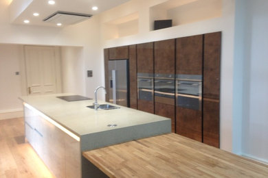This is an example of a large contemporary galley open plan kitchen in Edinburgh with flat-panel cabinets, with island, an undermount sink, concrete benchtops and light hardwood floors.