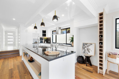 This is an example of a mid-sized modern l-shaped open plan kitchen in Brisbane with a double-bowl sink, white cabinets, laminate benchtops, window splashback, stainless steel appliances, medium hardwood floors, with island, multi-coloured floor and black benchtop.