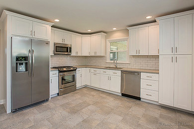 This is an example of a mid-sized transitional l-shaped open plan kitchen in Chicago with an undermount sink, shaker cabinets, white cabinets, white splashback, subway tile splashback, stainless steel appliances, no island and grey floor.