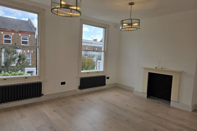 Inspiration for a small traditional enclosed living room in London with white walls, light hardwood flooring, a standard fireplace, a concrete fireplace surround, no tv, beige floors and feature lighting.