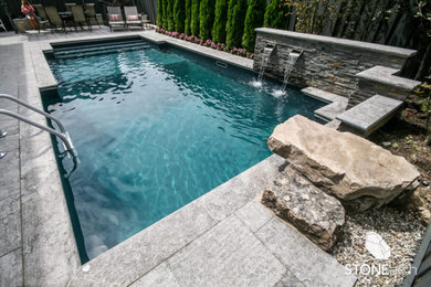 Imagen de piscina rectangular en patio trasero con adoquines de piedra natural