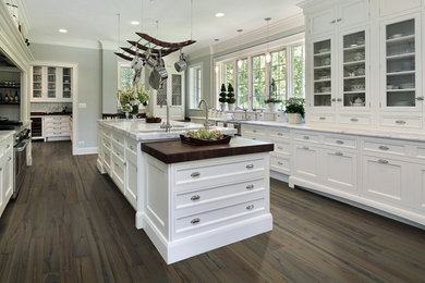 Example of a large transitional galley medium tone wood floor and brown floor kitchen pantry design in Los Angeles with a drop-in sink, an island, shaker cabinets, white cabinets, marble countertops, stainless steel appliances and white countertops