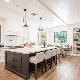 Transitional eat-in kitchen photos - Example of a transitional l-shaped medium tone wood floor and brown floor eat-in kitchen design in Los Angeles with shaker cabinets, white cabinets, white backsplash, subway tile backsplash, stainless steel appliances, an island and white countertops