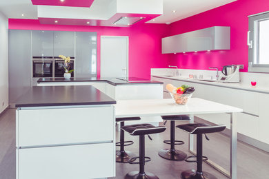 Cette image montre une grande cuisine ouverte minimaliste en L avec un placard à porte affleurante, des portes de placard blanches, un plan de travail en granite, 2 îlots, un évier intégré, une crédence blanche, un électroménager en acier inoxydable, un sol en carrelage de céramique, un sol gris et un plan de travail gris.