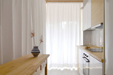 Diseño de cocina lineal actual de tamaño medio abierta con fregadero bajoencimera, armarios con paneles lisos, puertas de armario blancas, encimera de madera, salpicadero blanco, salpicadero de azulejos de cerámica, electrodomésticos de acero inoxidable, suelo de cemento y una isla