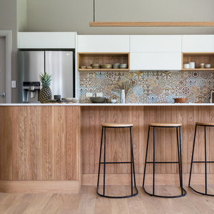 Idées déco pour une grande arrière-cuisine parallèle contemporaine avec un évier 2 bacs, un placard à porte plane, des portes de placard blanches, un plan de travail en surface solide, une crédence multicolore, une crédence en carreau de céramique, un électroménager en acier inoxydable, un sol en bois clair, un îlot central, un sol marron et un plan de travail blanc.