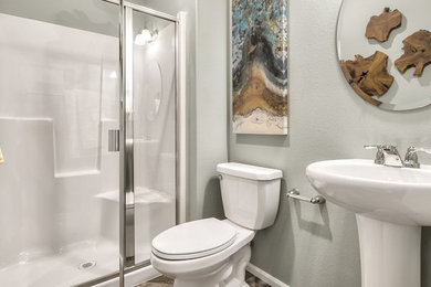 Example of a mid-sized eclectic 3/4 laminate floor and gray floor alcove shower design in Seattle with white cabinets, a one-piece toilet, gray walls, a pedestal sink and a hinged shower door