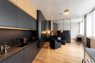 Design ideas for a small contemporary single-wall open plan kitchen in Paris with an integrated sink, beaded inset cabinets, black cabinets, solid surface benchtops, black splashback, panelled appliances, light hardwood floors, no island and black benchtop.