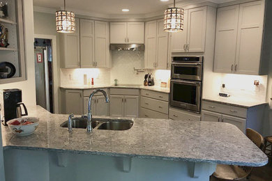 Transitional dark wood floor and brown floor kitchen photo in Raleigh with a double-bowl sink, recessed-panel cabinets, gray cabinets, granite countertops, white backsplash, porcelain backsplash and stainless steel appliances