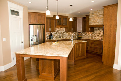 Example of a transitional u-shaped kitchen design in Cedar Rapids with a double-bowl sink, recessed-panel cabinets, medium tone wood cabinets, granite countertops, multicolored backsplash, stainless steel appliances and an island