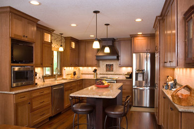 This is an example of a mid-sized arts and crafts u-shaped eat-in kitchen in Minneapolis with a double-bowl sink, flat-panel cabinets, medium wood cabinets, granite benchtops, beige splashback, stone tile splashback, stainless steel appliances, dark hardwood floors and with island.