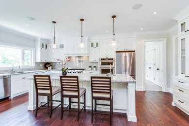 Example of a large classic l-shaped medium tone wood floor and brown floor eat-in kitchen design in Toronto with a double-bowl sink, recessed-panel cabinets, white cabinets, granite countertops, white backsplash, stainless steel appliances and an island