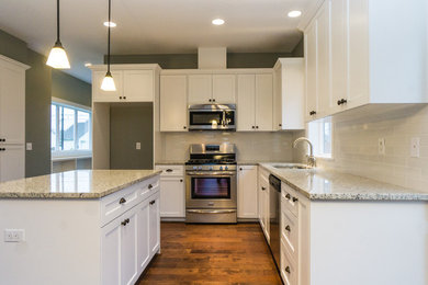 This is an example of a mid-sized traditional l-shaped eat-in kitchen in Portland with an undermount sink, recessed-panel cabinets, white cabinets, granite benchtops, white splashback, subway tile splashback, stainless steel appliances, medium hardwood floors and with island.