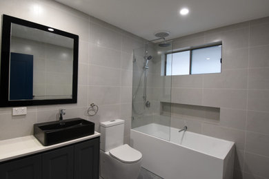 Photo of a mid-sized modern master bathroom in Sydney with shaker cabinets, grey cabinets, a freestanding tub, a shower/bathtub combo, a one-piece toilet, gray tile, porcelain tile, grey walls, ceramic floors, a console sink, engineered quartz benchtops, grey floor, an open shower and white benchtops.