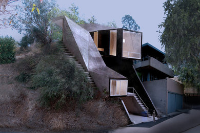 Cette photo montre une petite façade de maison noire tendance en béton à deux étages et plus avec un toit à croupette et un toit en métal.