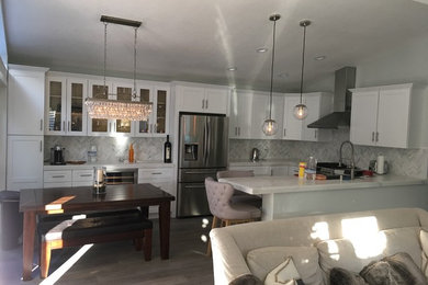 Medium sized modern single-wall kitchen/diner in Orange County with a belfast sink, shaker cabinets, white cabinets, engineered stone countertops, white splashback, ceramic splashback, stainless steel appliances, laminate floors and a breakfast bar.