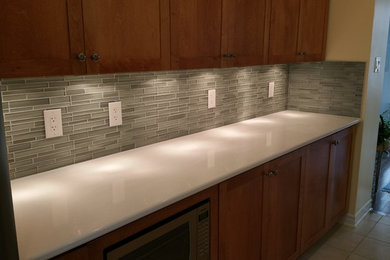Inspiration for a large ceramic tile kitchen remodel in Ottawa with an undermount sink, recessed-panel cabinets, dark wood cabinets, quartz countertops, gray backsplash, glass sheet backsplash, stainless steel appliances and an island