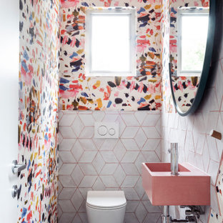 Immagine di un piccolo bagno di servizio minimal con WC monopezzo, piastrelle bianche, piastrelle in gres porcellanato, pareti multicolore, pavimento in cemento, lavabo sospeso, top in cemento, pavimento nero, top rosa, mobile bagno sospeso e carta da parati