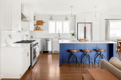 Example of a large mid-century modern medium tone wood floor and brown floor eat-in kitchen design in Minneapolis with an undermount sink, shaker cabinets, white cabinets, quartz countertops, white backsplash, subway tile backsplash, stainless steel appliances, an island and white countertops