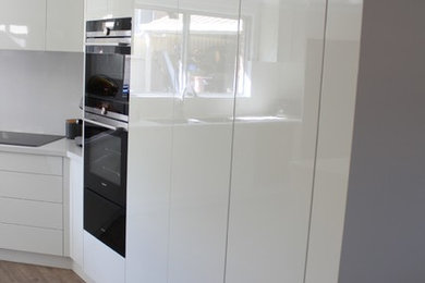 This is an example of a large modern eat-in kitchen in Sydney with an undermount sink, white cabinets, granite benchtops, white splashback, glass sheet splashback, black appliances, laminate floors, with island, brown floor and white benchtop.