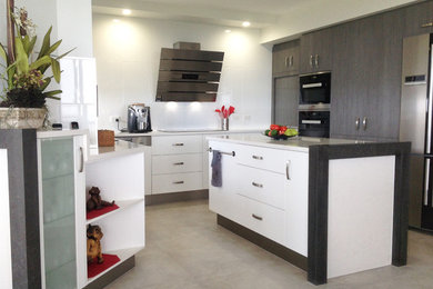 This is an example of a large modern u-shaped kitchen pantry in Gold Coast - Tweed with quartz benchtops, white splashback, stainless steel appliances, with island, white floor, a drop-in sink, flat-panel cabinets, white cabinets, ceramic splashback and ceramic floors.