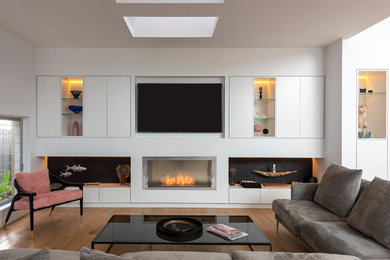 This is an example of a large contemporary open concept living room in Sydney with white walls, light hardwood floors, a standard fireplace, a plaster fireplace surround and a built-in media wall.
