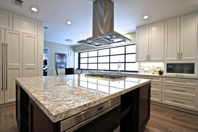 Example of a transitional u-shaped medium tone wood floor and brown floor open concept kitchen design in Orange County with an undermount sink, recessed-panel cabinets, white cabinets, mosaic tile backsplash, stainless steel appliances and an island
