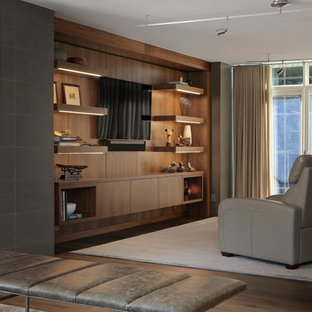 Cette photo montre une salle de cinéma tendance fermée et de taille moyenne avec un mur gris, un sol en bois foncé, un téléviseur fixé au mur et un sol marron.