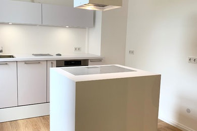 Large contemporary kitchen in Frankfurt with an integrated sink, flat-panel cabinets, white cabinets, white splashback, stainless steel appliances, medium hardwood floors, with island, brown floor and white benchtop.