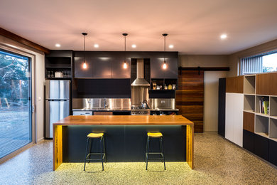 This is an example of a small contemporary galley kitchen in Sydney with an integrated sink, open cabinets, stainless steel cabinets, wood benchtops, metallic splashback, stainless steel appliances, concrete floors and with island.