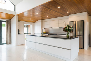 Mid-sized contemporary galley kitchen in Christchurch with an undermount sink, flat-panel cabinets, white cabinets, quartz benchtops, grey splashback, glass sheet splashback, stainless steel appliances, ceramic floors, with island and white floor.