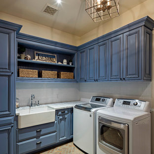 フェニックスの中サイズの地中海スタイルのおしゃれな洗濯室 (エプロンフロントシンク、レイズドパネル扉のキャビネット、青いキャビネット、珪岩カウンター、ベージュの壁、レンガの床、左右配置の洗濯機・乾燥機) の写真