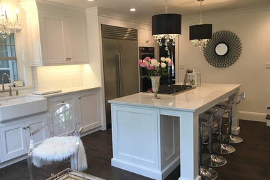 Inspiration for a large timeless porcelain tile and brown floor kitchen remodel in New York with a farmhouse sink, flat-panel cabinets, white cabinets, quartz countertops, white backsplash, subway tile backsplash, stainless steel appliances, an island and white countertops