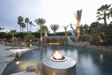 This is an example of a tropical backyard custom-shaped pool in Orange County with a water feature and natural stone pavers.