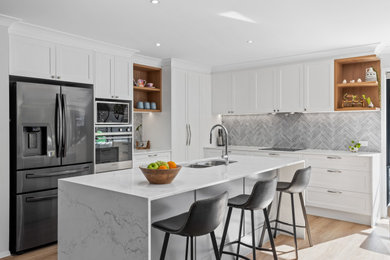 Photo of a mid-sized modern u-shaped open plan kitchen in Gold Coast - Tweed with an undermount sink, shaker cabinets, white cabinets, quartz benchtops, grey splashback, ceramic splashback, black appliances, vinyl floors, with island, brown floor, white benchtop and recessed.