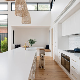 Inspiration för mellanstora moderna vitt kök, med en rustik diskho, skåp i shakerstil, vita skåp, bänkskiva i kvarts, vitt stänkskydd, stänkskydd i keramik, rostfria vitvaror, mellanmörkt trägolv, en köksö och brunt golv