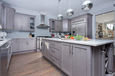 Large transitional l-shaped medium tone wood floor and brown floor enclosed kitchen photo in Bridgeport with an undermount sink, shaker cabinets, gray cabinets, quartzite countertops, gray backsplash, ceramic backsplash, stainless steel appliances, an island and white countertops