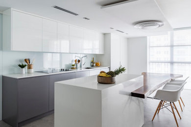 Inspiration for a contemporary open plan kitchen in Miami with an undermount sink, flat-panel cabinets, white cabinets, solid surface benchtops, white splashback, glass sheet splashback, white appliances, concrete floors, with island and grey floor.