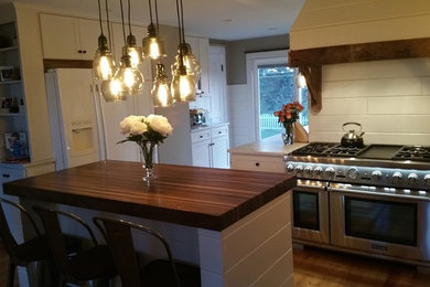 Eat-in kitchen - large light wood floor eat-in kitchen idea in New York with recessed-panel cabinets, white cabinets, wood countertops, white backsplash, stainless steel appliances and an island
