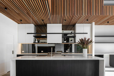Large contemporary galley open plan kitchen in Melbourne with flat-panel cabinets, mirror splashback, stainless steel appliances, concrete floors, with island, grey floor, grey benchtop, a double-bowl sink, solid surface benchtops and grey splashback.