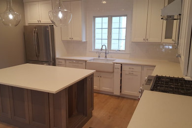 Inspiration for a mid-sized country l-shaped brown floor and dark wood floor eat-in kitchen remodel in New York with a farmhouse sink, white cabinets, quartz countertops, white backsplash, subway tile backsplash, stainless steel appliances, an island and recessed-panel cabinets