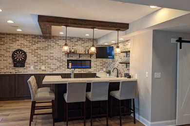 Large transitional walk-out vinyl floor, brown floor, exposed beam and brick wall basement photo in Other with a bar, gray walls, a standard fireplace and a brick fireplace