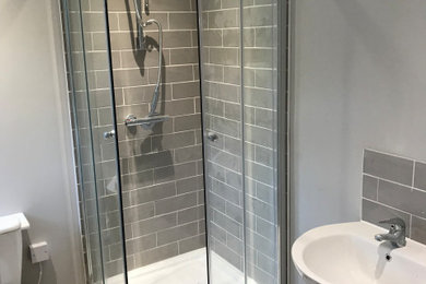 This is an example of a small modern grey and white ensuite bathroom in London with a corner shower, a one-piece toilet, grey tiles, ceramic tiles, grey walls, a pedestal sink, a sliding door and a single sink.
