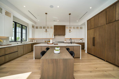 Example of a large minimalist galley light wood floor and brown floor eat-in kitchen design in Los Angeles with white backsplash, ceramic backsplash, white appliances, two islands and white countertops