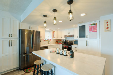 Mid-sized elegant laminate floor and beige floor open concept kitchen photo in Other with an integrated sink, shaker cabinets, white cabinets, solid surface countertops, white backsplash, subway tile backsplash, stainless steel appliances, an island and white countertops