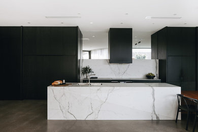 Contemporary galley eat-in kitchen in Adelaide with an undermount sink, flat-panel cabinets, black cabinets, white splashback, panelled appliances, concrete floors, with island, grey floor and white benchtop.