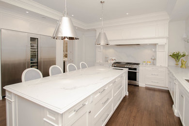 Open concept kitchen - huge traditional l-shaped dark wood floor and brown floor open concept kitchen idea in Other with an undermount sink, recessed-panel cabinets, white cabinets, quartz countertops, gray backsplash, marble backsplash, stainless steel appliances and an island