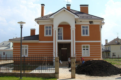 Diseño de fachada de casa roja tradicional renovada de tamaño medio de dos plantas con revestimiento de estuco, tejado a cuatro aguas y tejado de teja de barro
