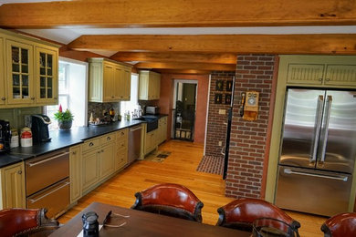 Inspiration for a mid-sized country galley medium tone wood floor and brown floor eat-in kitchen remodel in New York with a farmhouse sink, beaded inset cabinets, green cabinets, soapstone countertops, brown backsplash, mosaic tile backsplash, stainless steel appliances and no island