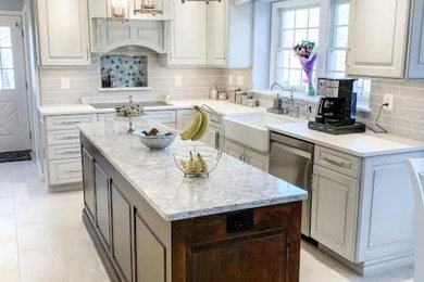 Mid-sized transitional l-shaped porcelain tile and beige floor eat-in kitchen photo in Baltimore with a farmhouse sink, raised-panel cabinets, white cabinets, quartz countertops, gray backsplash, ceramic backsplash, stainless steel appliances, an island and white countertops
